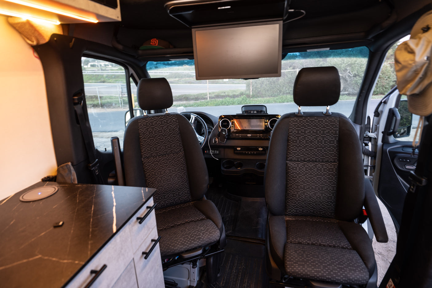 Inside a modern rv rental van, showing the front seats, dashboard, ceiling screen, and a custom interior counter.
