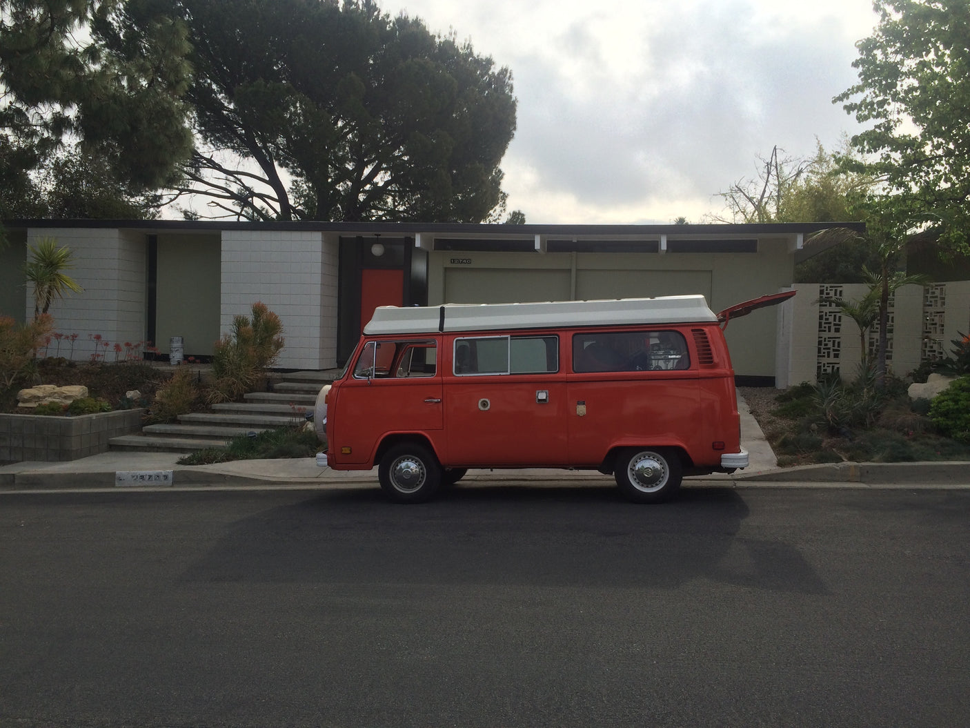 This vibrant orange VW camper van, perfect for an RV rental experience, is parked in front of a stylish modern home.