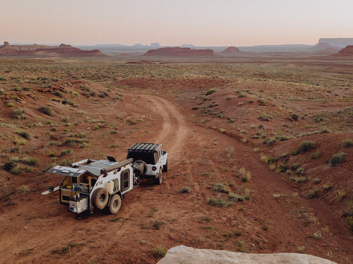 Explore the desert! This white Jeep pulls an off-road RV rental, its rear kitchen open for remote adventure camping.