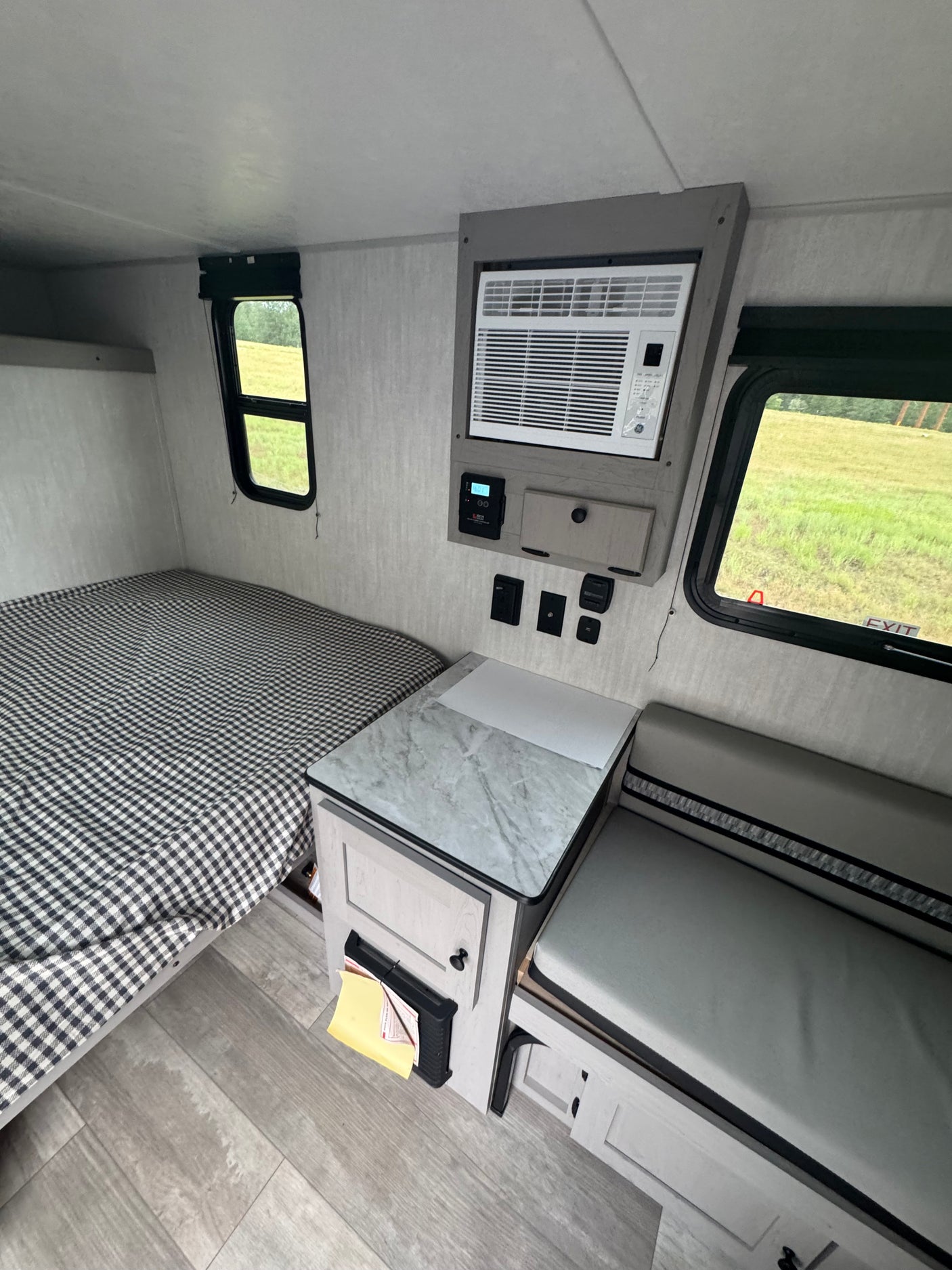 This RV rental's interior boasts a comfortable bed, wall-mounted AC unit, dinette, and bright windows with green outdoor scenery.