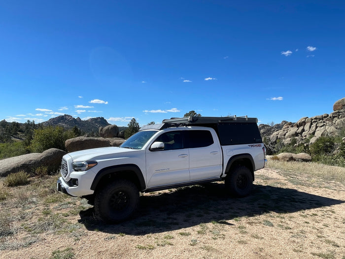 A white Toyota Tacoma with a truck bed camper parked in a scenic rocky landscape, ideal for an RV rental adventure.