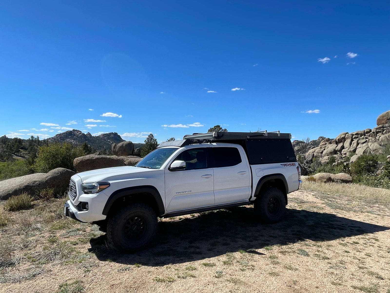 A white Toyota Tacoma with a truck bed camper parked in a scenic rocky landscape, ideal for an RV rental adventure.