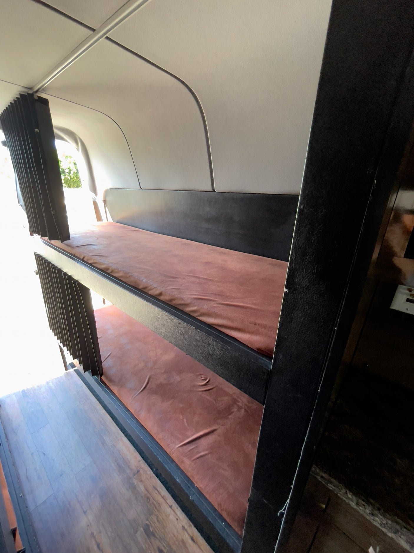 RV rental bunk beds. View inside a camper van showing two brown-mattressed bunks and window shades.