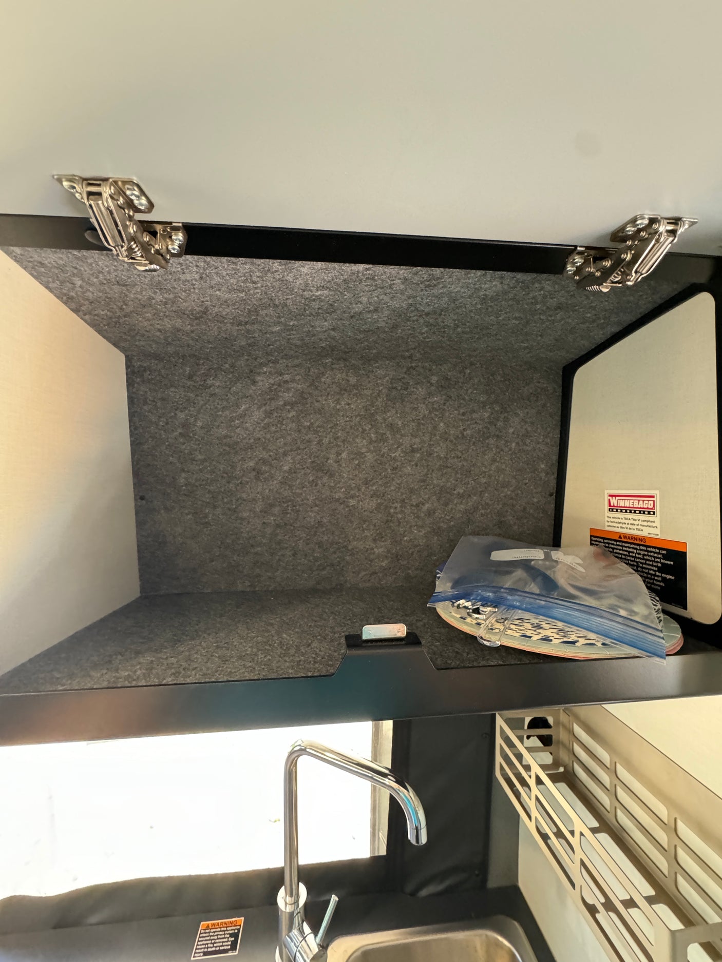 Inside an RV rental: storage cabinet with hinges above a kitchen sink, showing compact organization for essential items.