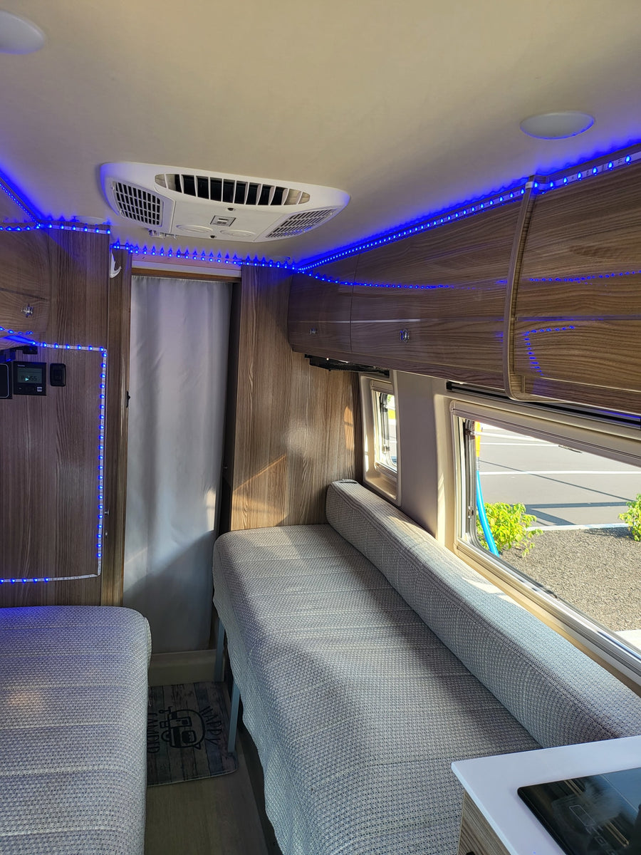 Interior of an **rv rental** showing a cozy living space with bright blue LED lights, a ceiling AC unit, and wood cabinetry.