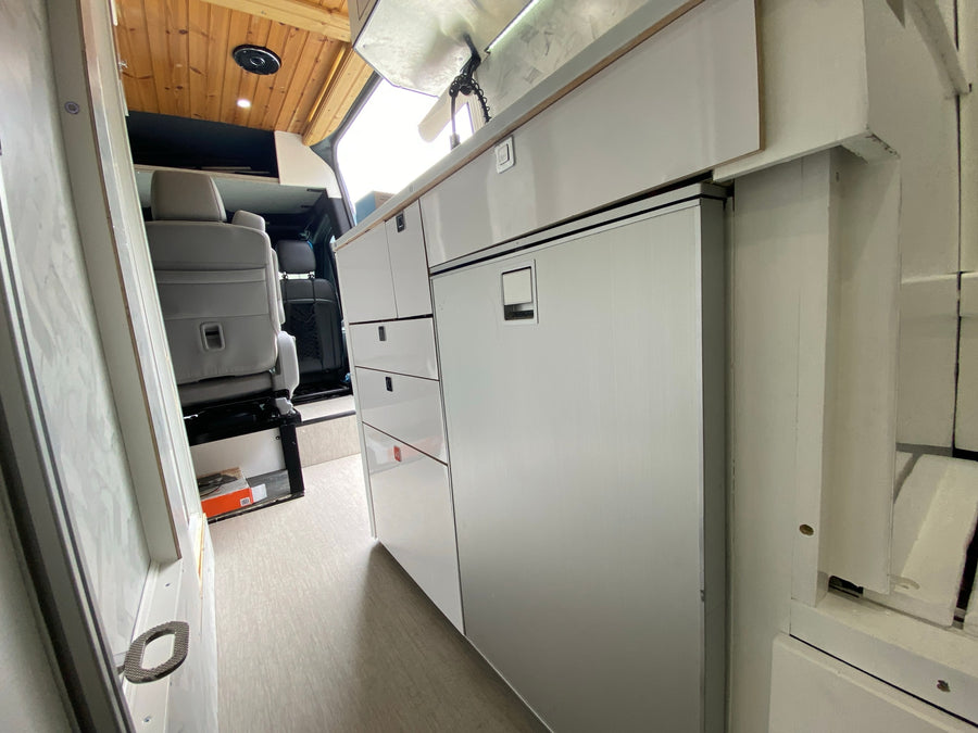 aiding parking by showing the vehicle and its surroundings.|RV rental interior: Sleek white camper van kitchen with fridge