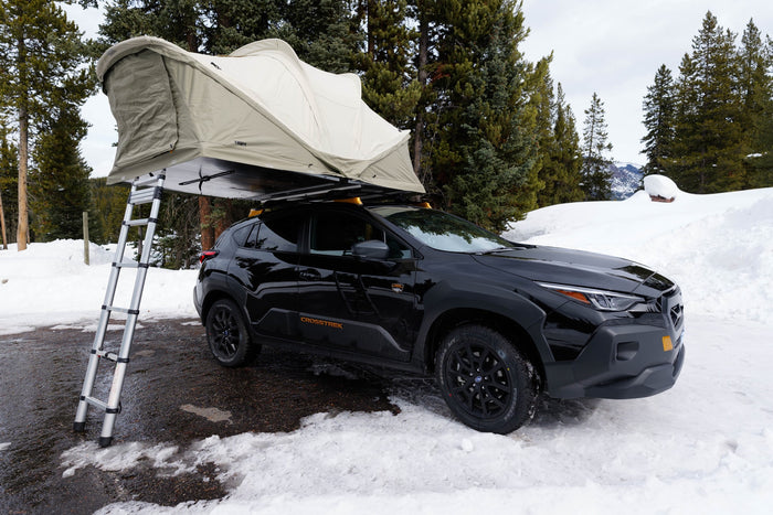 Black Subaru Crosstrek with rooftop tent parked in snow. This setup offers versatile outdoor camping, a great alternative to an rv rental.
