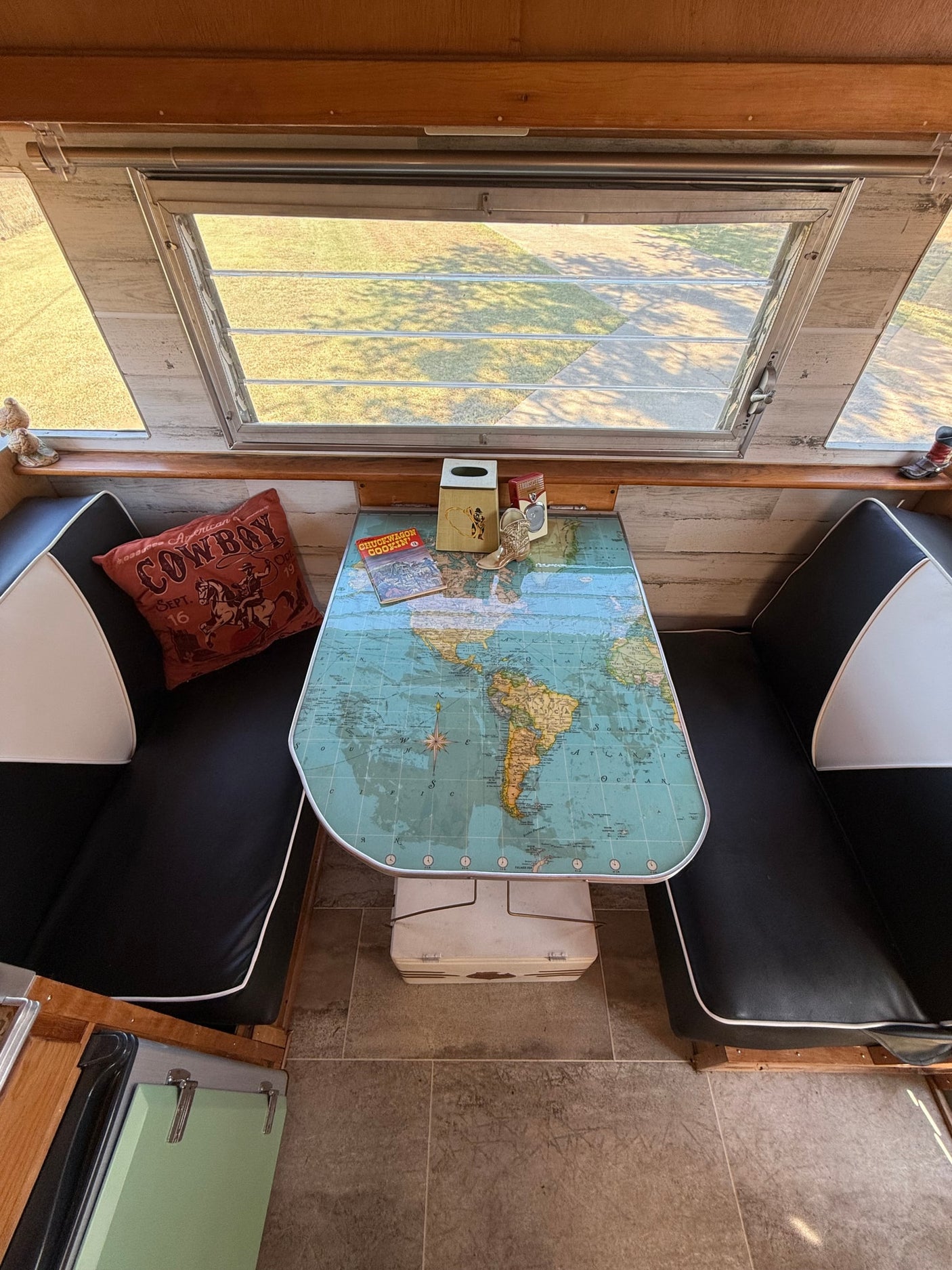 An RV rental's inviting dinette features a world map table, comfy black and white benches, and western-themed accents.