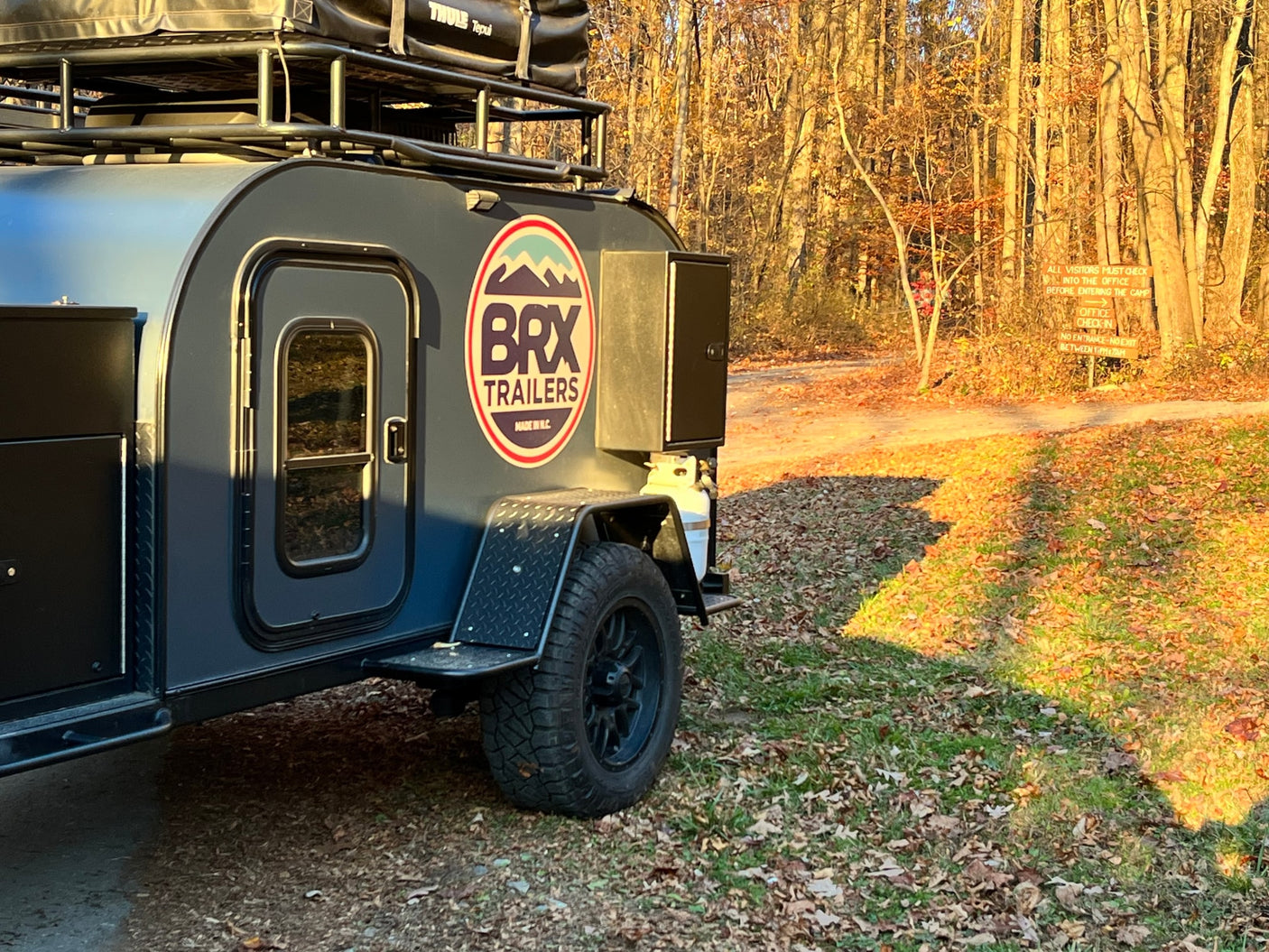 Off-road adventure: Man by campfire with a Jeep & teardrop camper. Explore with an RV rental like this!|This RV rental setup features a black Jeep Gladiator towing a BRX overlanding trailer with a rooftop tent by a scenic mountain lake.|Jeep Gladiator tows a rugged RV rental trailer with a man standing atop