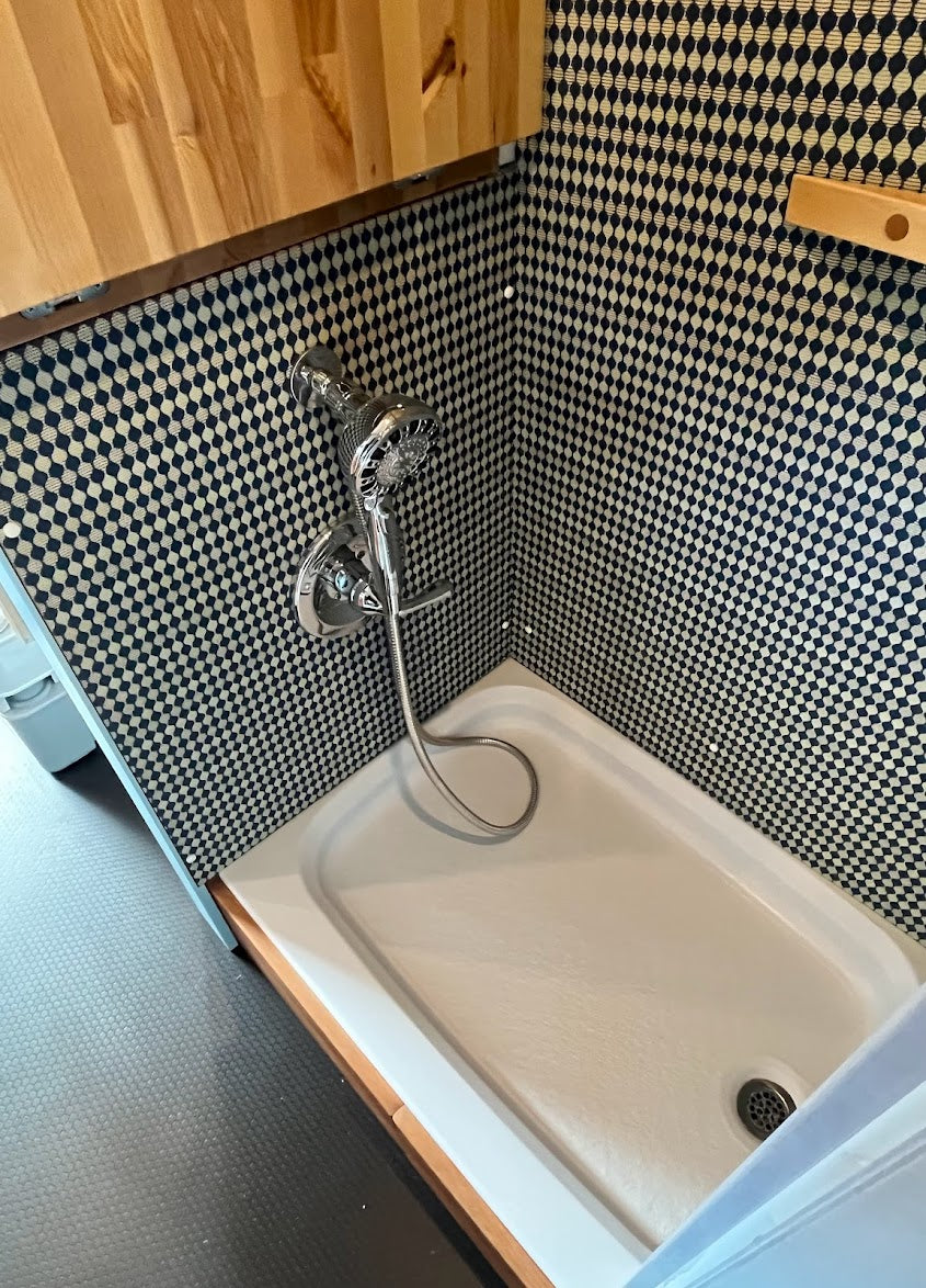 Modern RV rental shower with checkerboard walls, chrome shower head, and white pan. Compact and functional design.