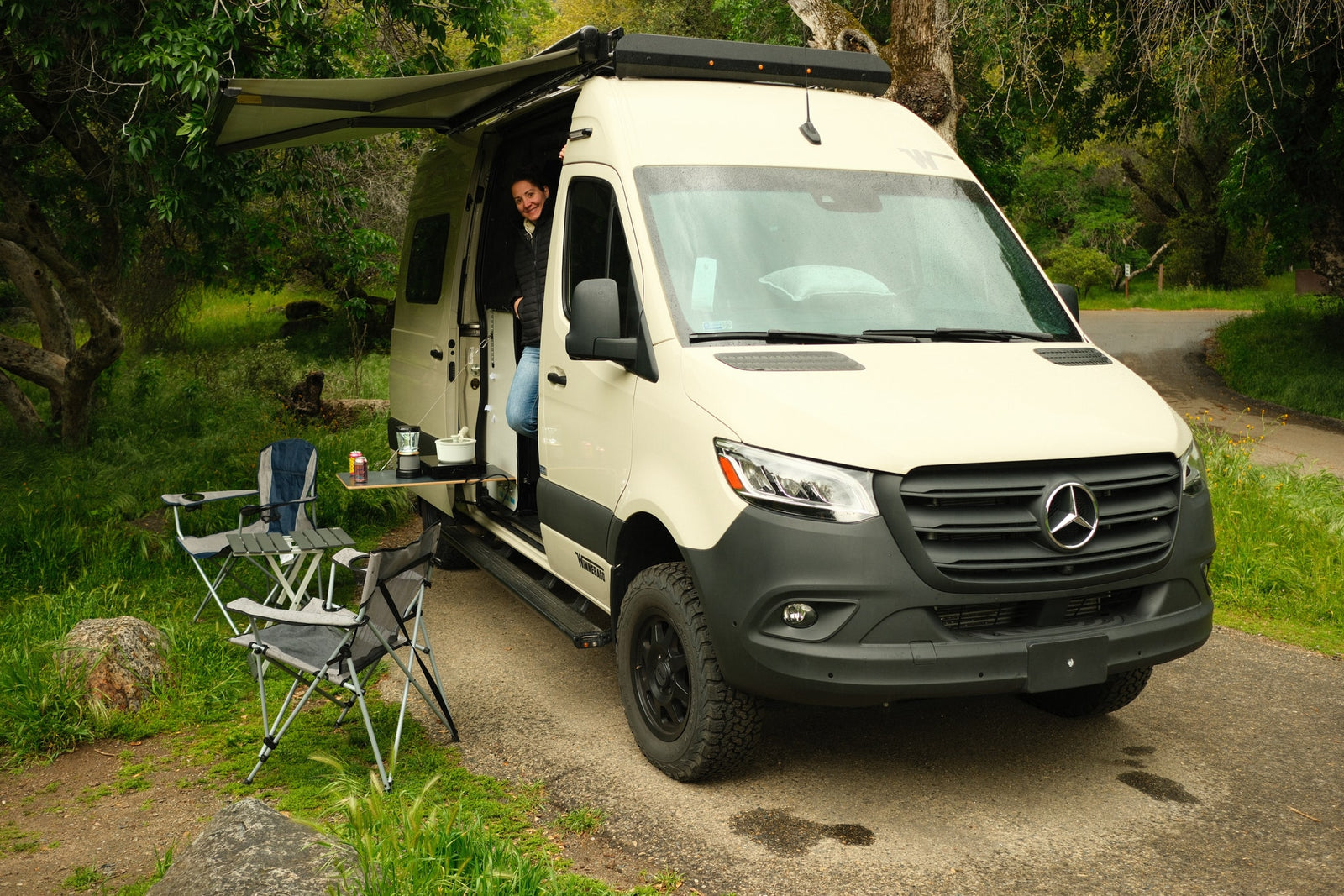 surrounded by green grass & yellow wildflowers.|Perfect rv rental for nature trips! Woman in camper van doorway