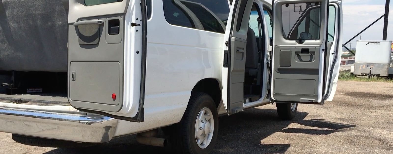 This white RV rental van has its rear and side doors open, revealing its cargo area and interior.