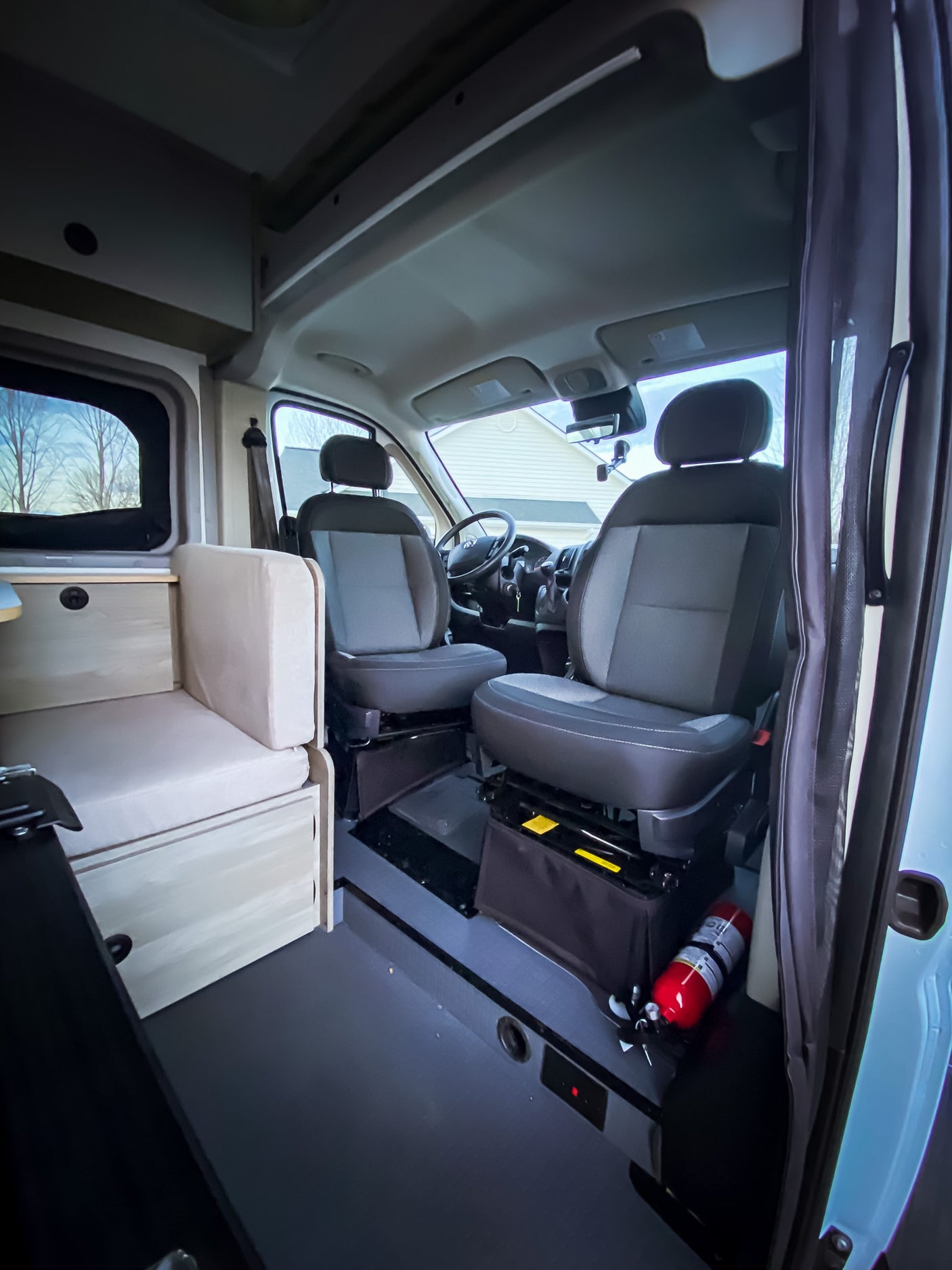 This RV rental shows a camper van's front seats, a light wood bench, and a red fire extinguisher on the floor.