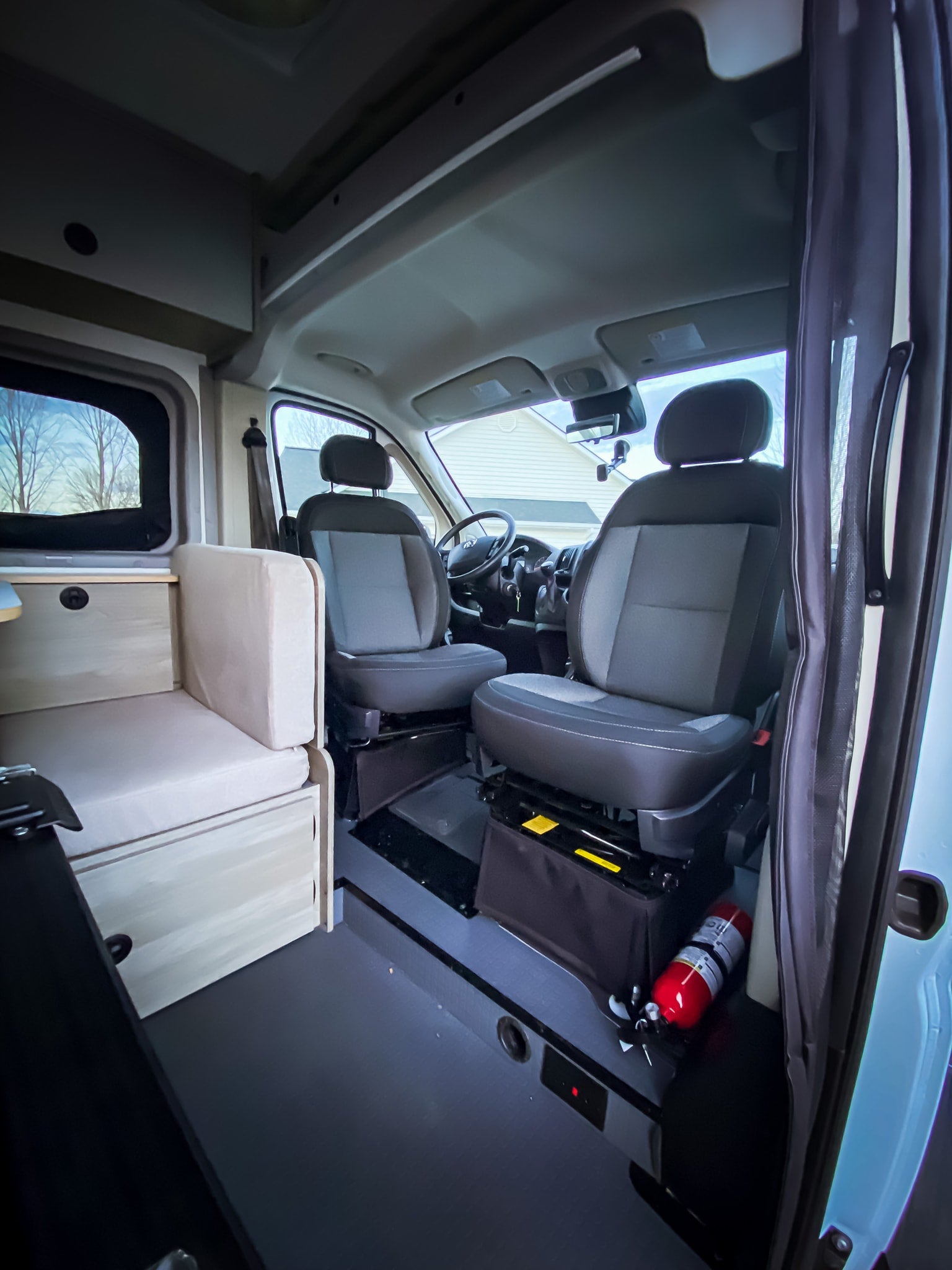 This RV rental shows a camper van's front seats, a light wood bench, and a red fire extinguisher on the floor.