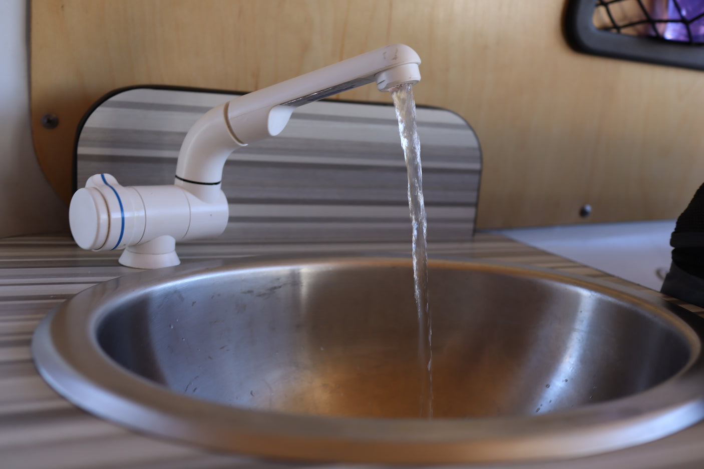 Water flows from a white faucet into a stainless steel sink, showcasing the compact kitchen in an RV rental.