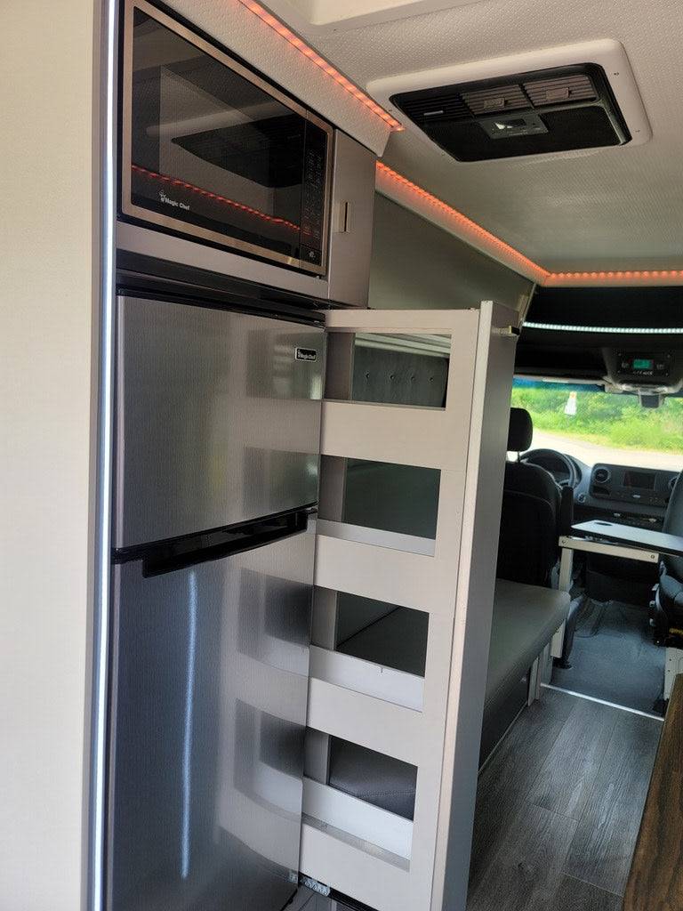 RV rental: Compact kitchen featuring a stainless steel microwave, refrigerator, and a clever pull-out pantry in a modern camper.