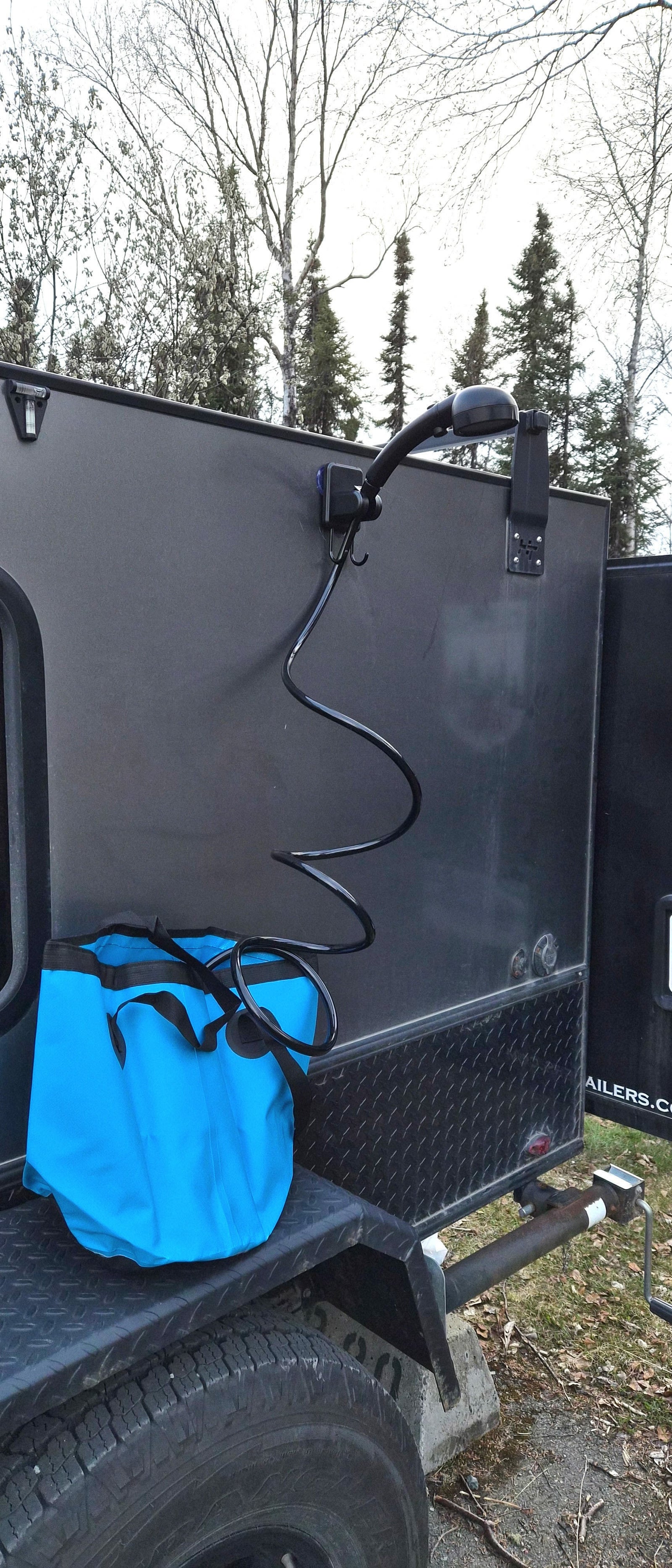 Outdoor shower on an rv rental trailer, featuring a coiled hose & blue bucket. Ideal for camping & road trips.