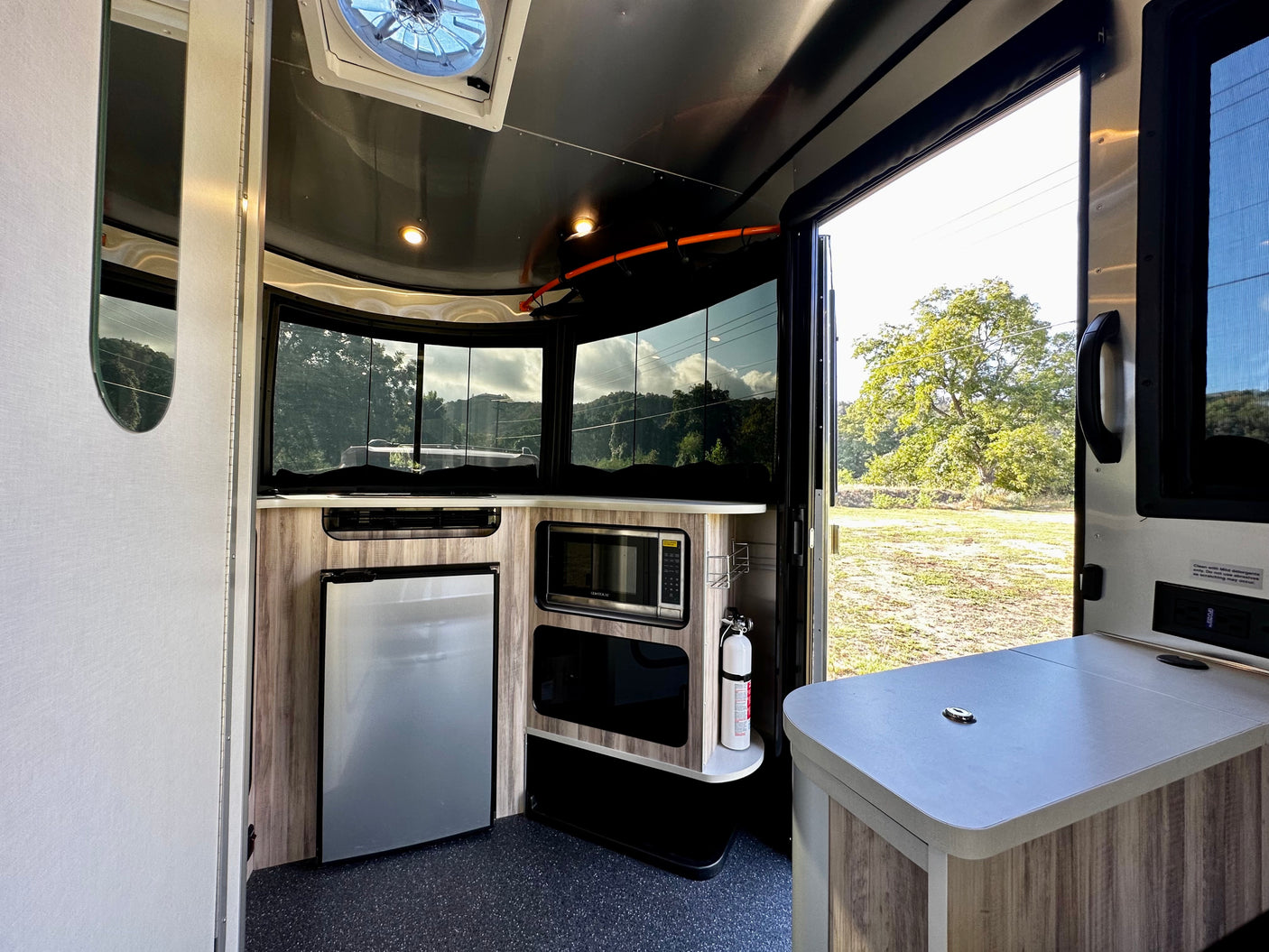 This RV rental interior features a compact kitchen with fridge, microwave, and counter, offering scenic outdoor views.