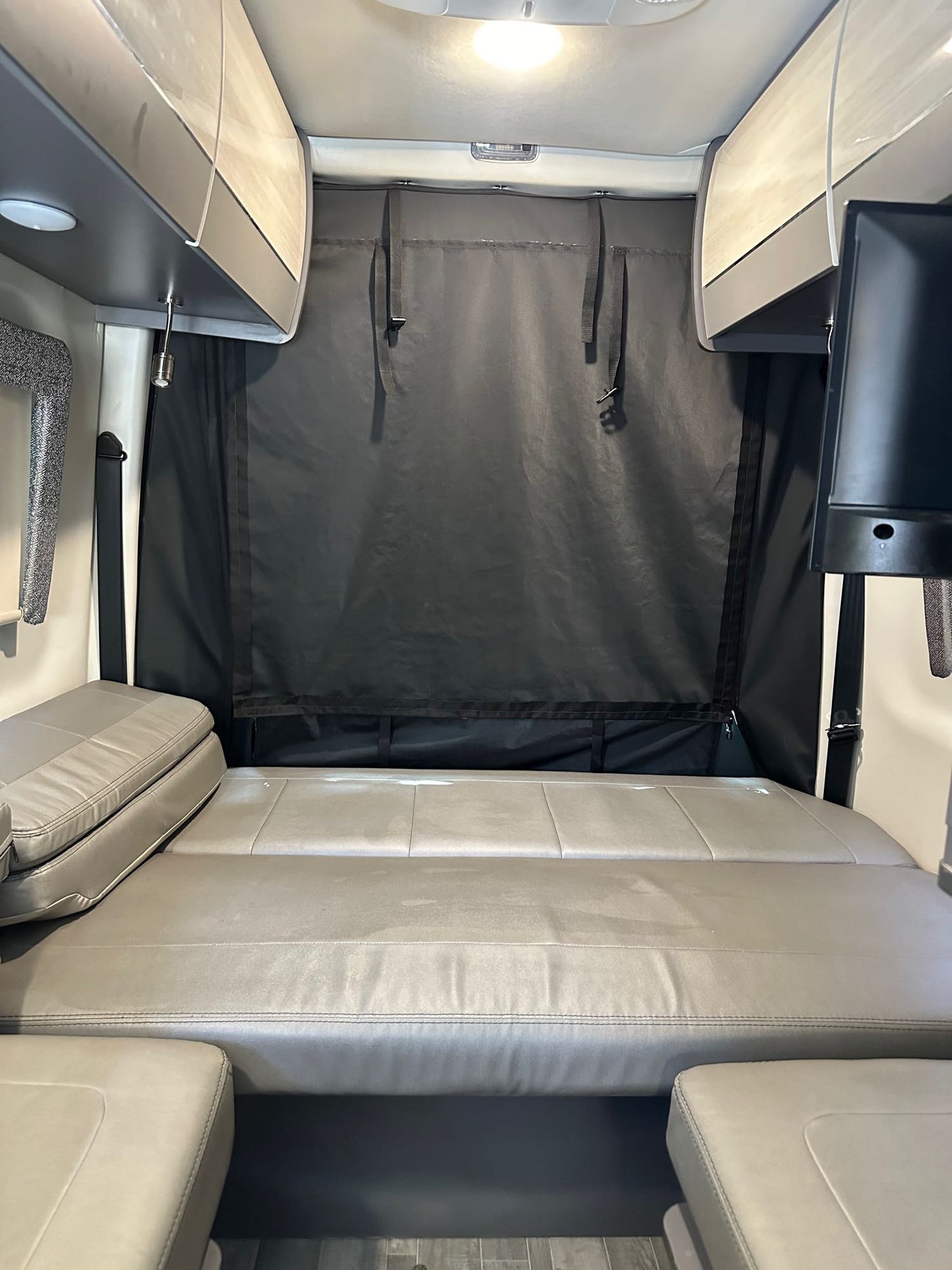 Spacious RV rental interior featuring a comfy bed, overhead storage, privacy curtain, and TV, perfect for your next road trip.