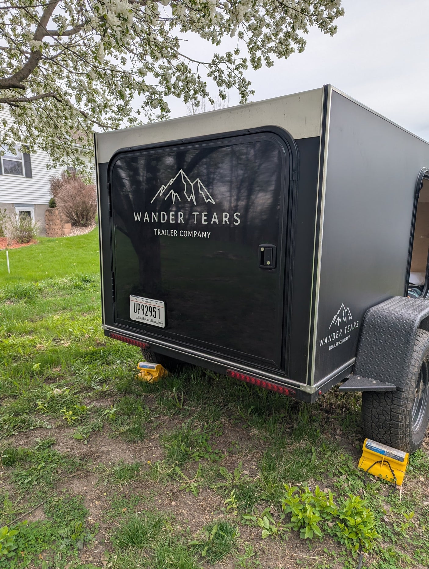 Black Wander Tears teardrop trailer, great for RV rental or camping, securely parked on grass with wheel chocks.