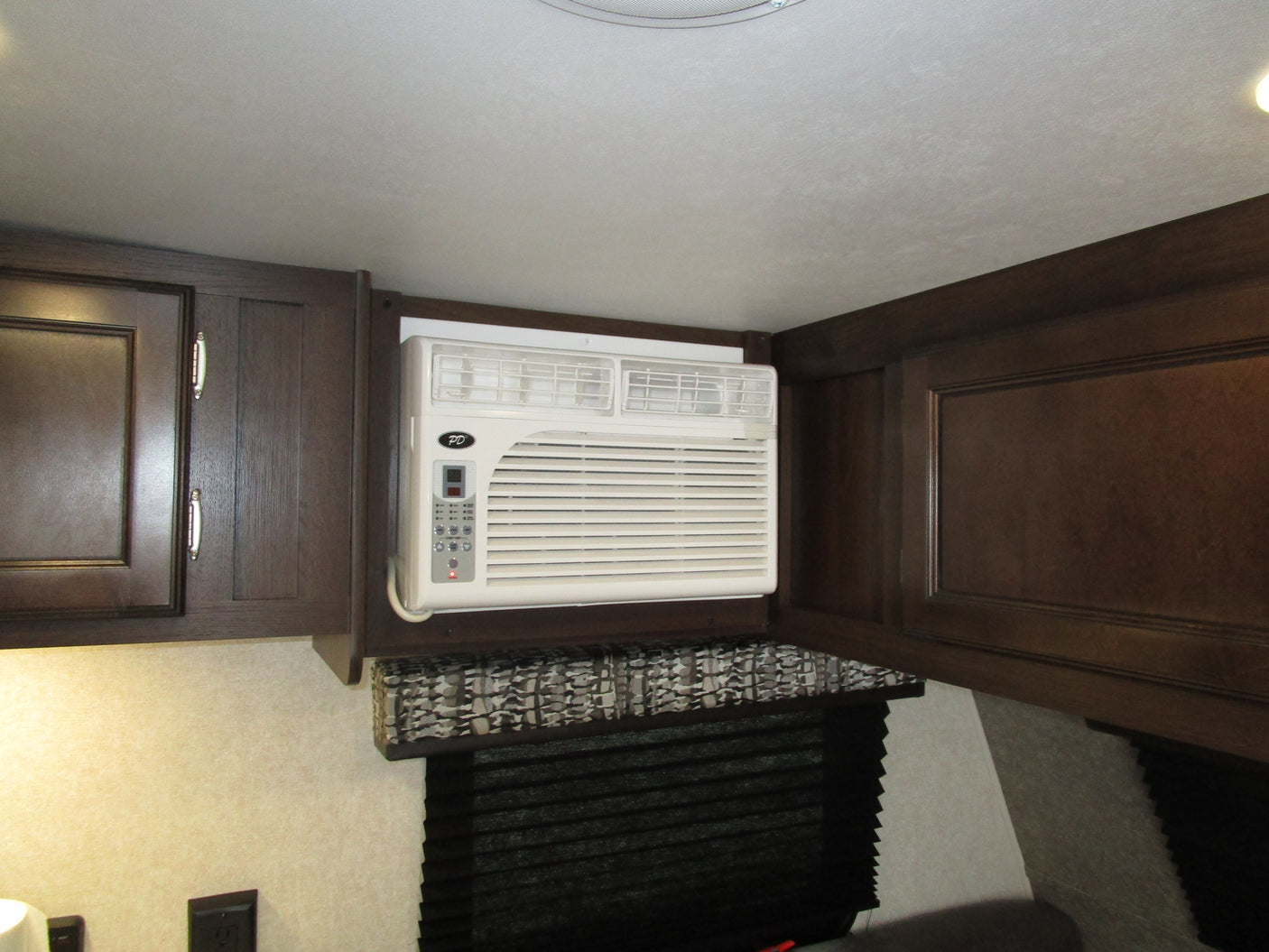 Compact RV rental interior featuring dark wood cabinets and a built-in air conditioner for a comfortable stay.