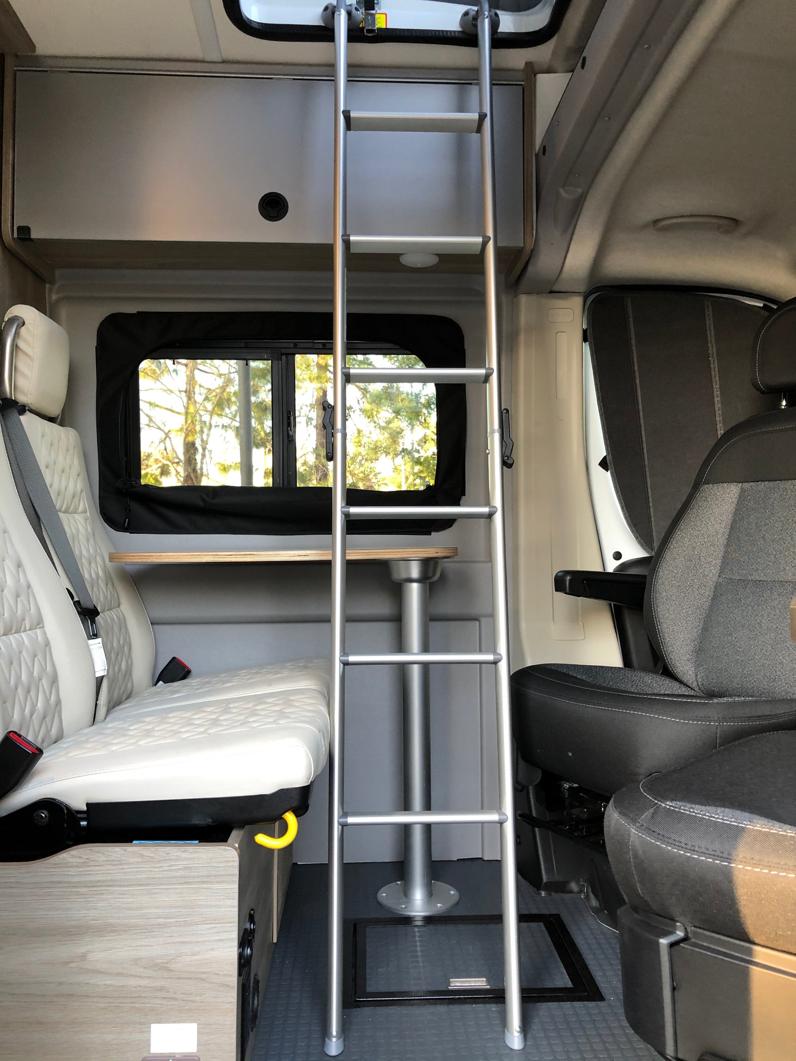 Spacious RV rental interior featuring a ladder, quilted seating, and a versatile dining table for compact living.