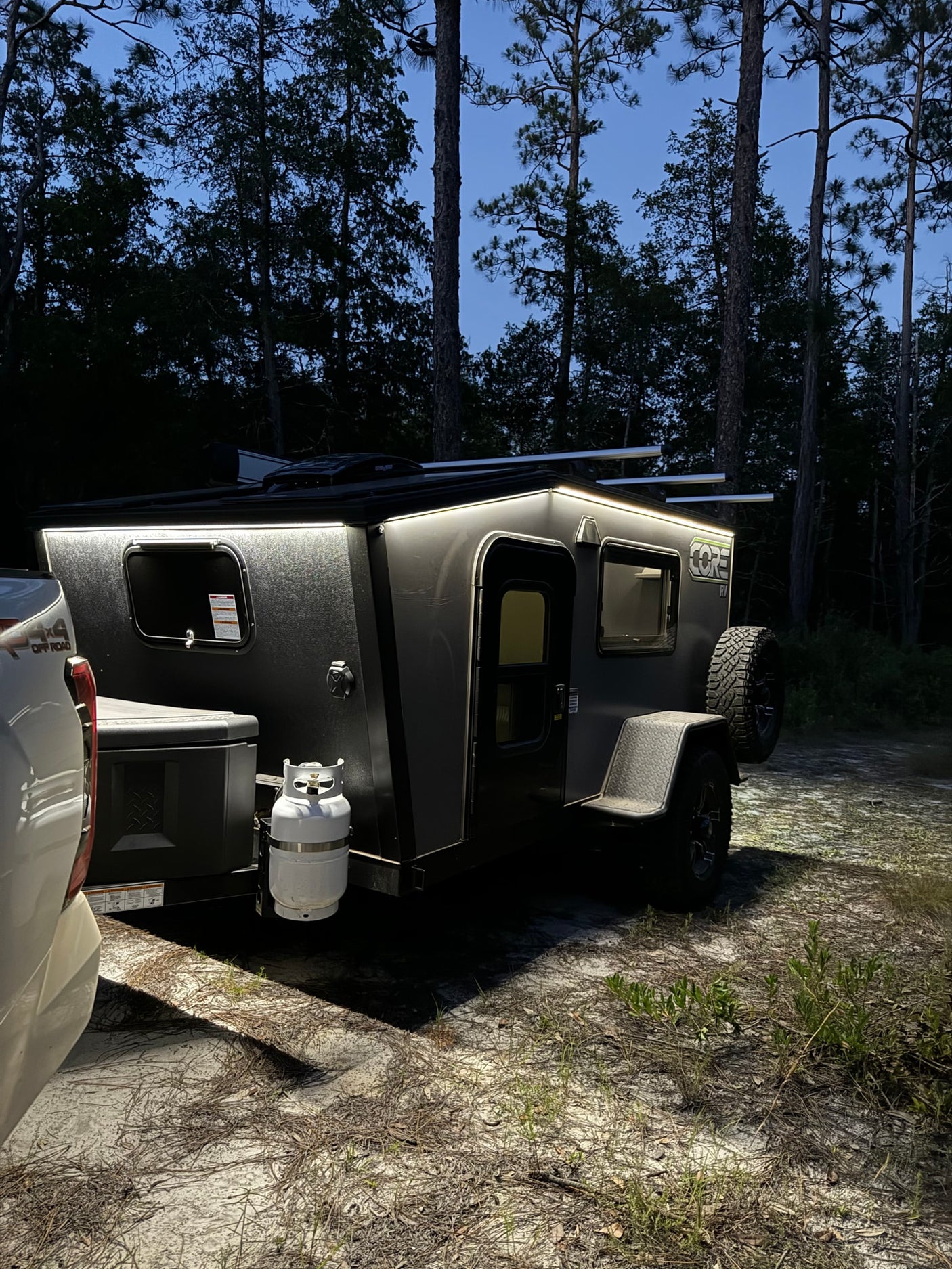 parked in a forest campsite with a truck.|A CORE RV rental trailer