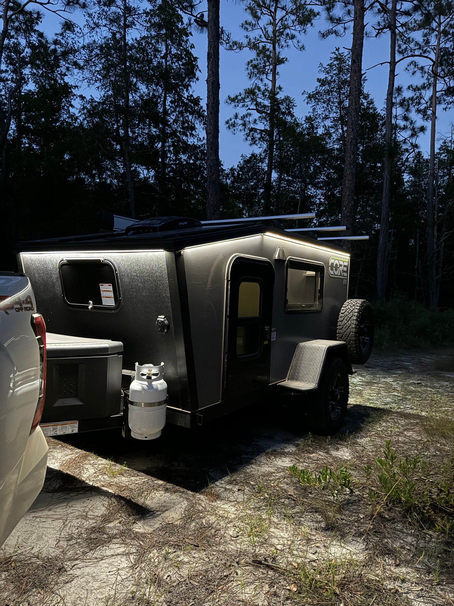 parked in a forest campsite with a truck.|A CORE RV rental trailer