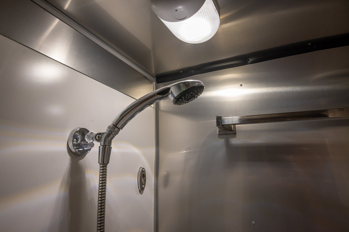 RV rental shower: A compact, brightly lit stall with a chrome shower head and sleek metallic/white walls for travel.