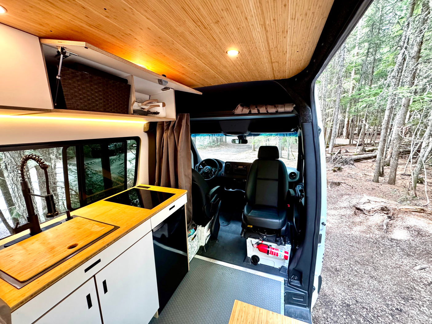 Modern RV rental interior featuring a compact kitchen, comfortable seating, and a serene forest view. Ideal for travel.