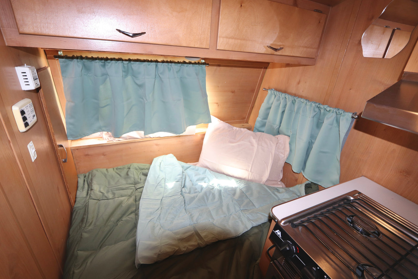 Experience this cozy RV rental's bedroom and kitchen. Features wooden interior, soft bedding, and natural light.