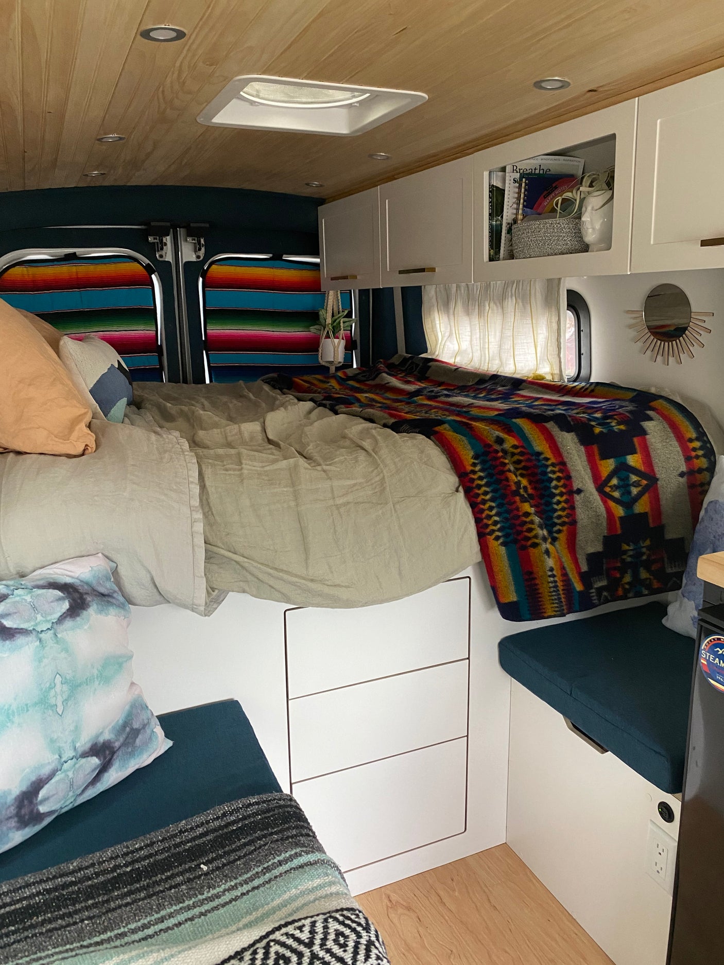 Cozy RV rental interior featuring a comfy bed with colorful blankets, overhead storage, and a wooden ceiling.