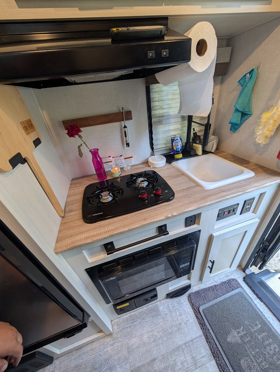 A well-equipped rv rental kitchen showing a two-burner stovetop, sink, microwave, and range hood, perfect for small space living.