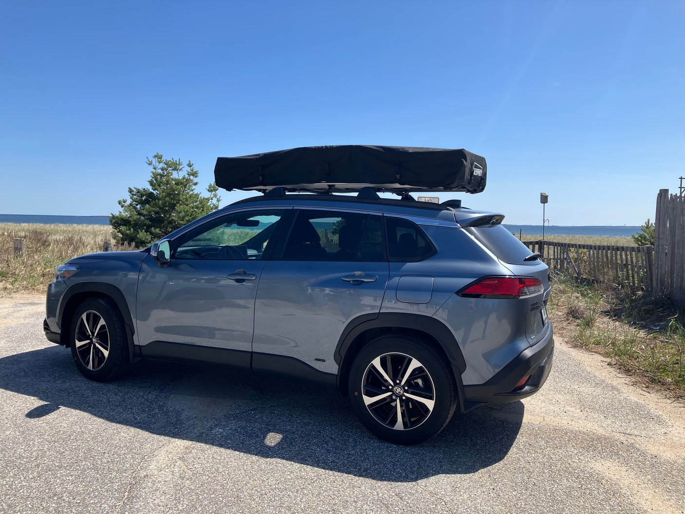 Gray SUV with rooftop tent, parked by the ocean, ready for adventure. A flexible travel setup, like a compact RV rental alternative.