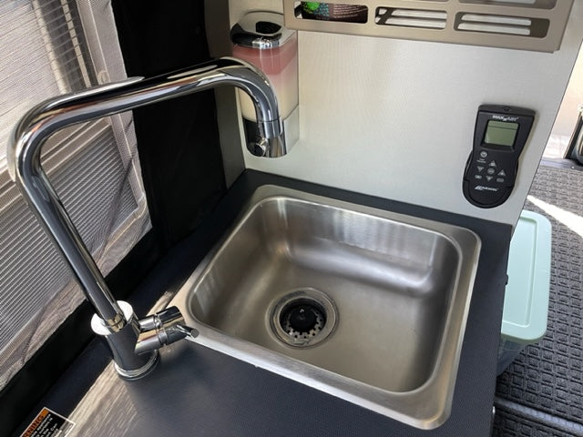 Compact RV rental kitchen features a stainless steel sink, chrome faucet, and a wall-mounted control panel.