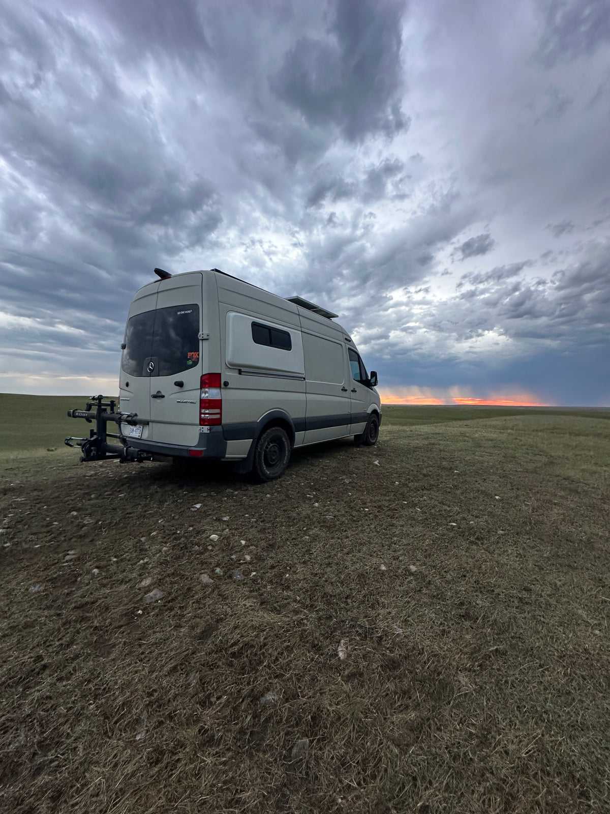 RV rental van parked in a vast field under a dramatic cloudy sky with a sunset horizon. Perfect for adventure! — photo 4