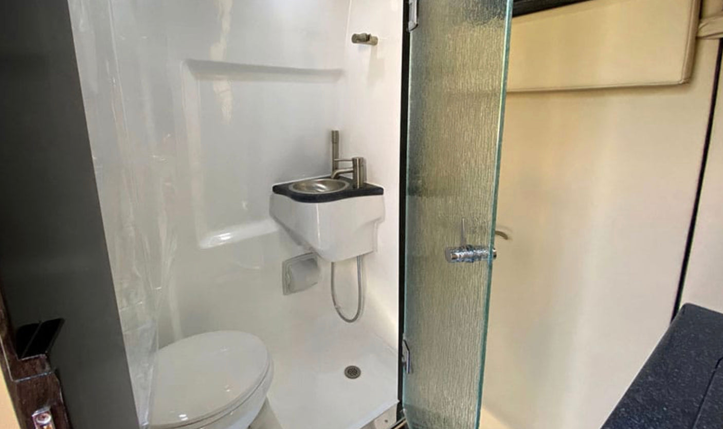 This RV rental offers a compact, functional bathroom featuring a toilet, wall-mounted sink, and shower with glass door.
