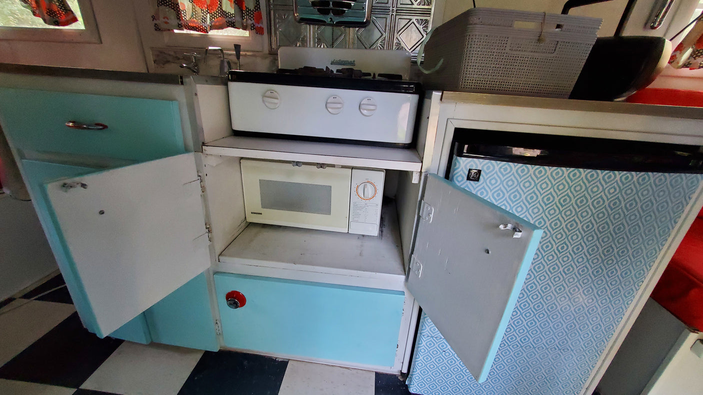 RV rental kitchen: White stovetop, Samsung microwave, light blue cabinets, and patterned fridge area. Functional and compact.
