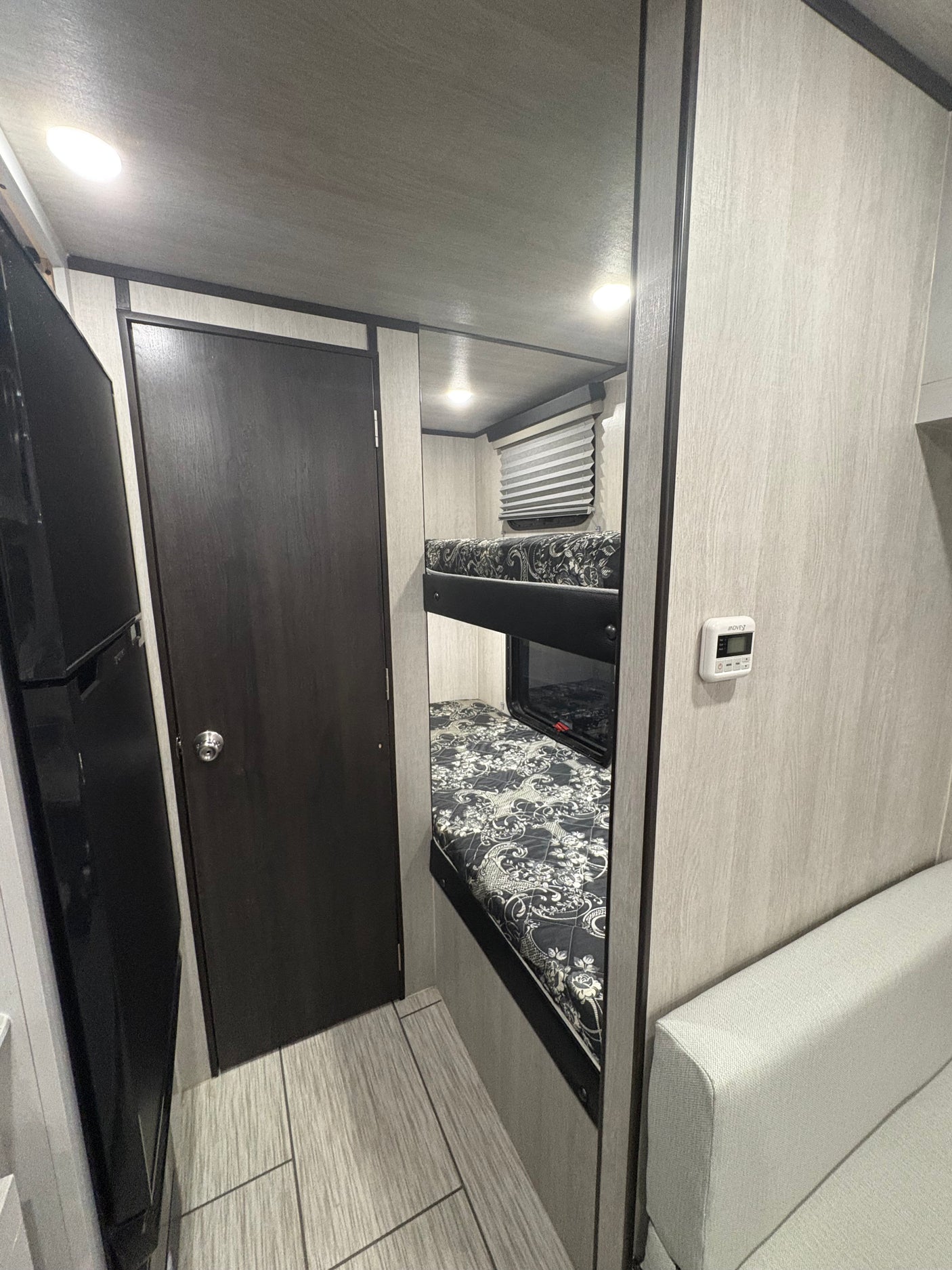 RV rental interior: two bunk beds, refrigerator, and light couch, showcasing a compact and functional layout.
