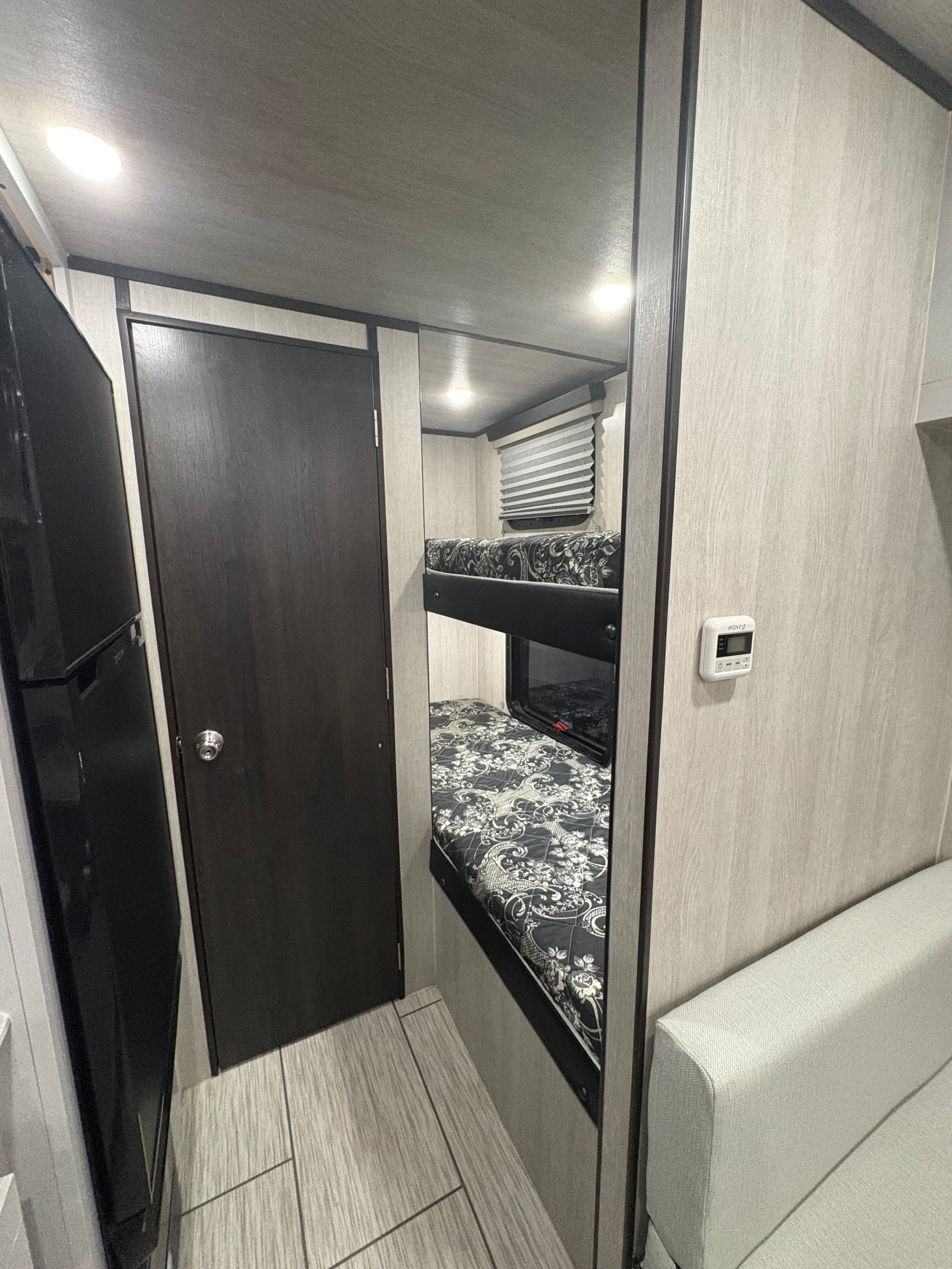RV rental interior: two bunk beds, refrigerator, and light couch, showcasing a compact and functional layout.