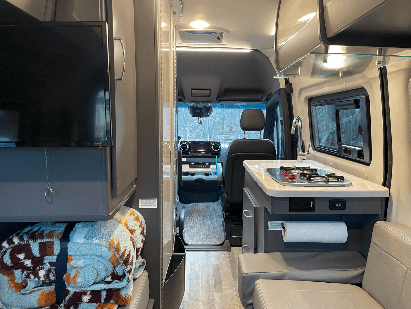 Step inside this modern rv rental camper van, featuring a compact kitchen, comfortable living area, and front cockpit for travel.