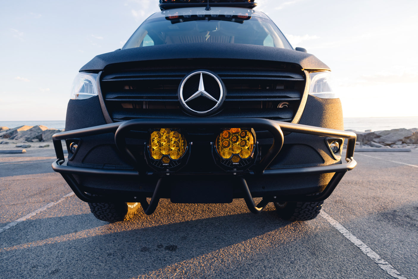 Front view of a custom black Mercedes-Benz Sprinter adventure van, featuring yellow off-road lights and a rugged bumper. Ideal for an RV rental.