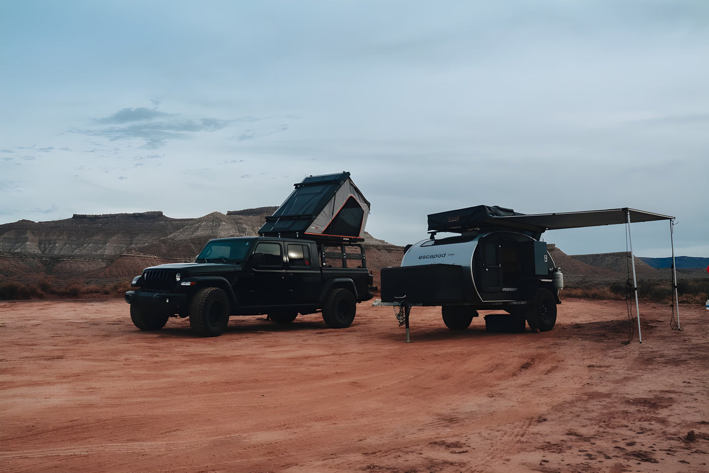 Explore with an RV rental: Black Jeep Gladiator, roof-top tent, & Escapod trailer set up for overlanding in the desert.