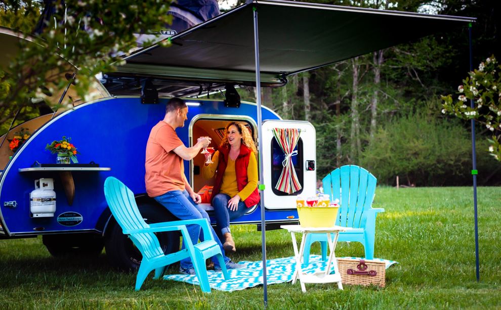 adults relax.|An RV rental provides the perfect camping trip. A couple relaxes with drinks by their blue teardrop camper under its awning.|Two happy people in a rooftop tent on a blue teardrop RV rental