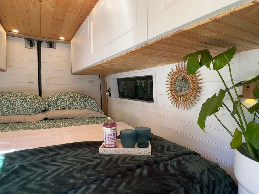 showing a kitchen setup in the foreground.|Modern RV rental interior with a cozy bed
