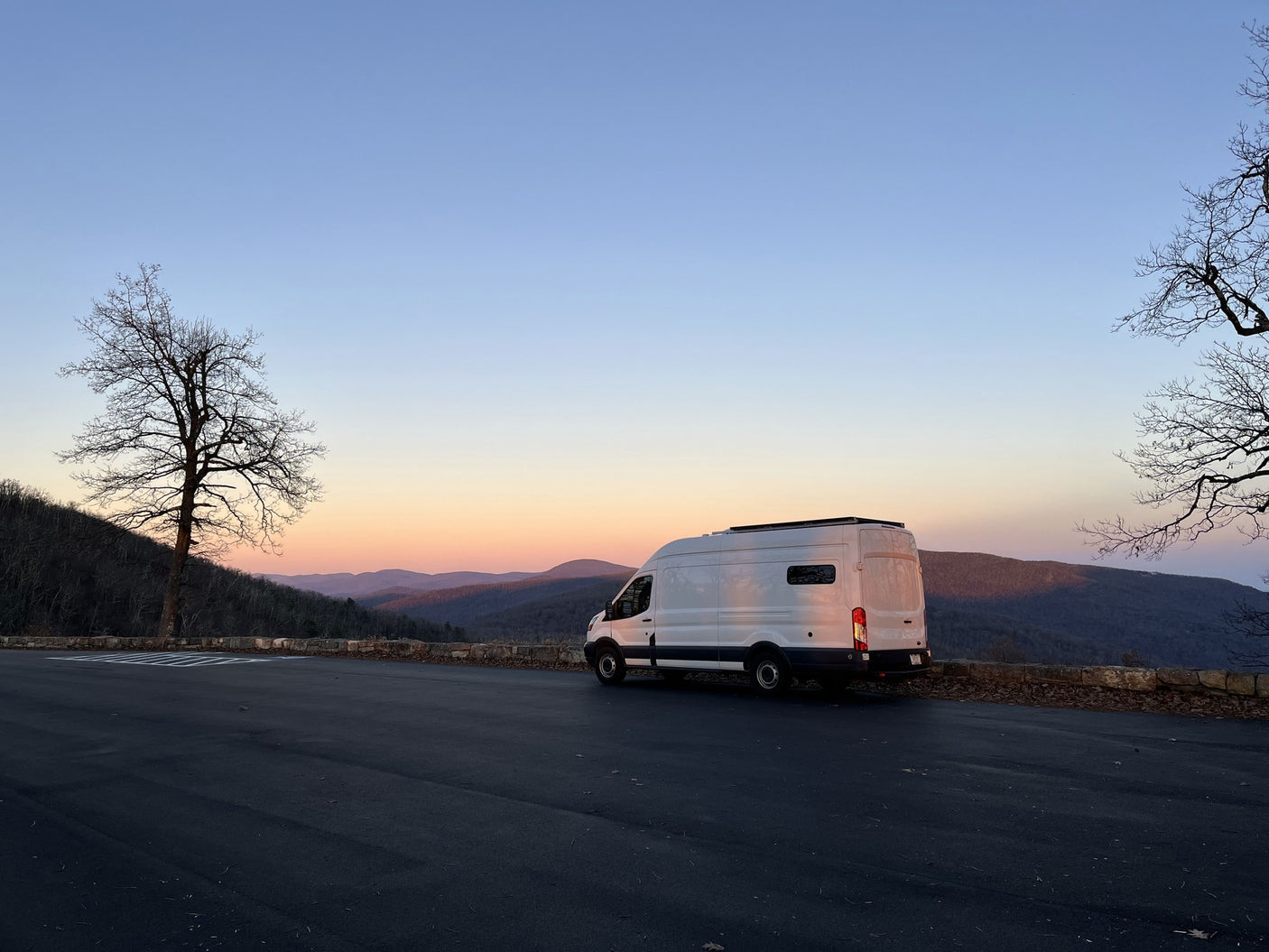 A white rv rental camper van overlooks a tranquil mountain range during a soft sunset