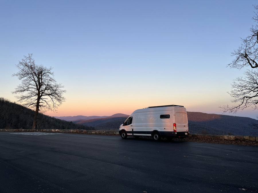 A white rv rental camper van overlooks a tranquil mountain range during a soft sunset