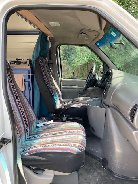 RV rental van interior, showing colorful patterned front seats and a custom bed area behind for travelers.