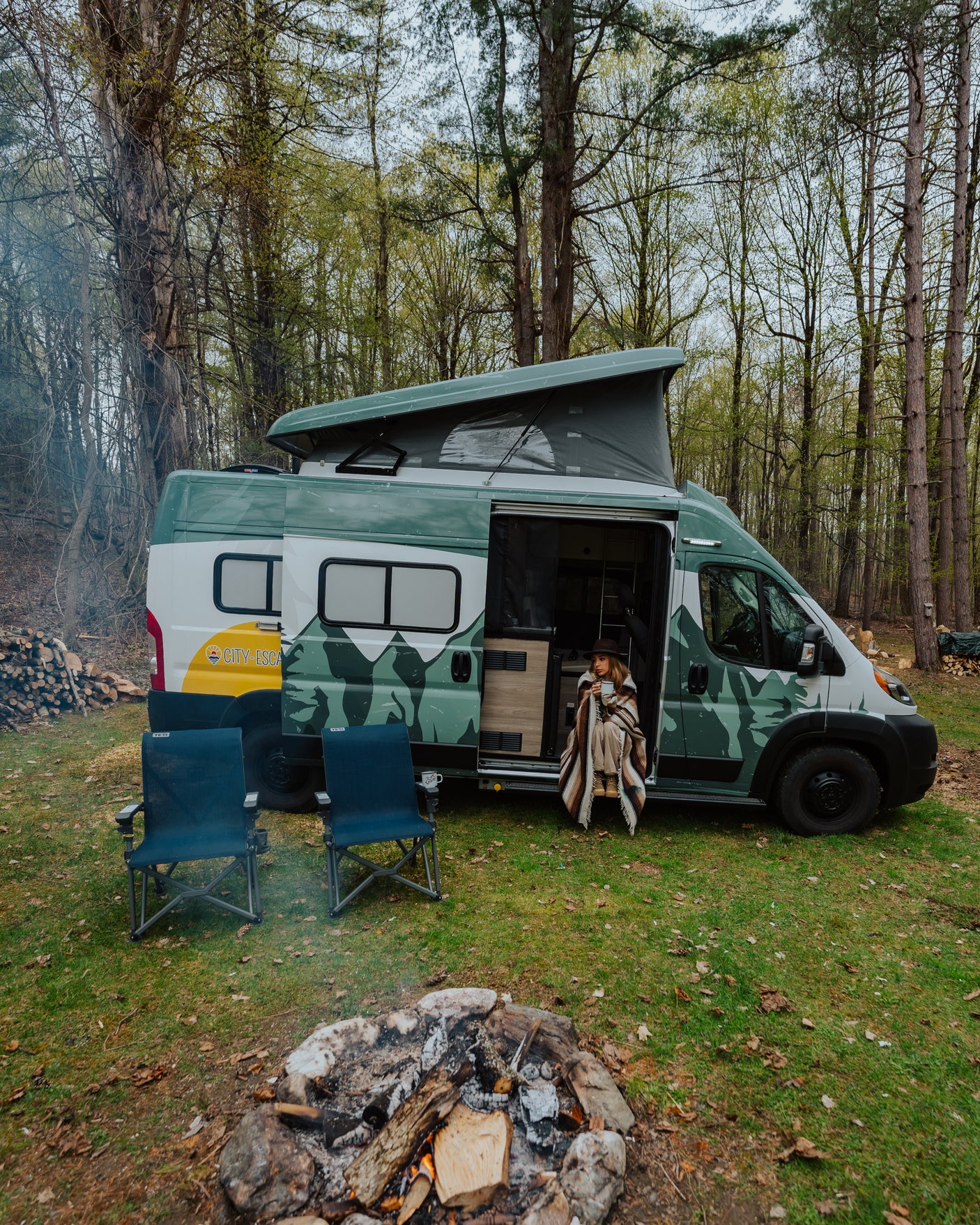 Cozy rv rental experience: a pop-top camper van with a person relaxing, chairs, and a crackling campfire in nature.