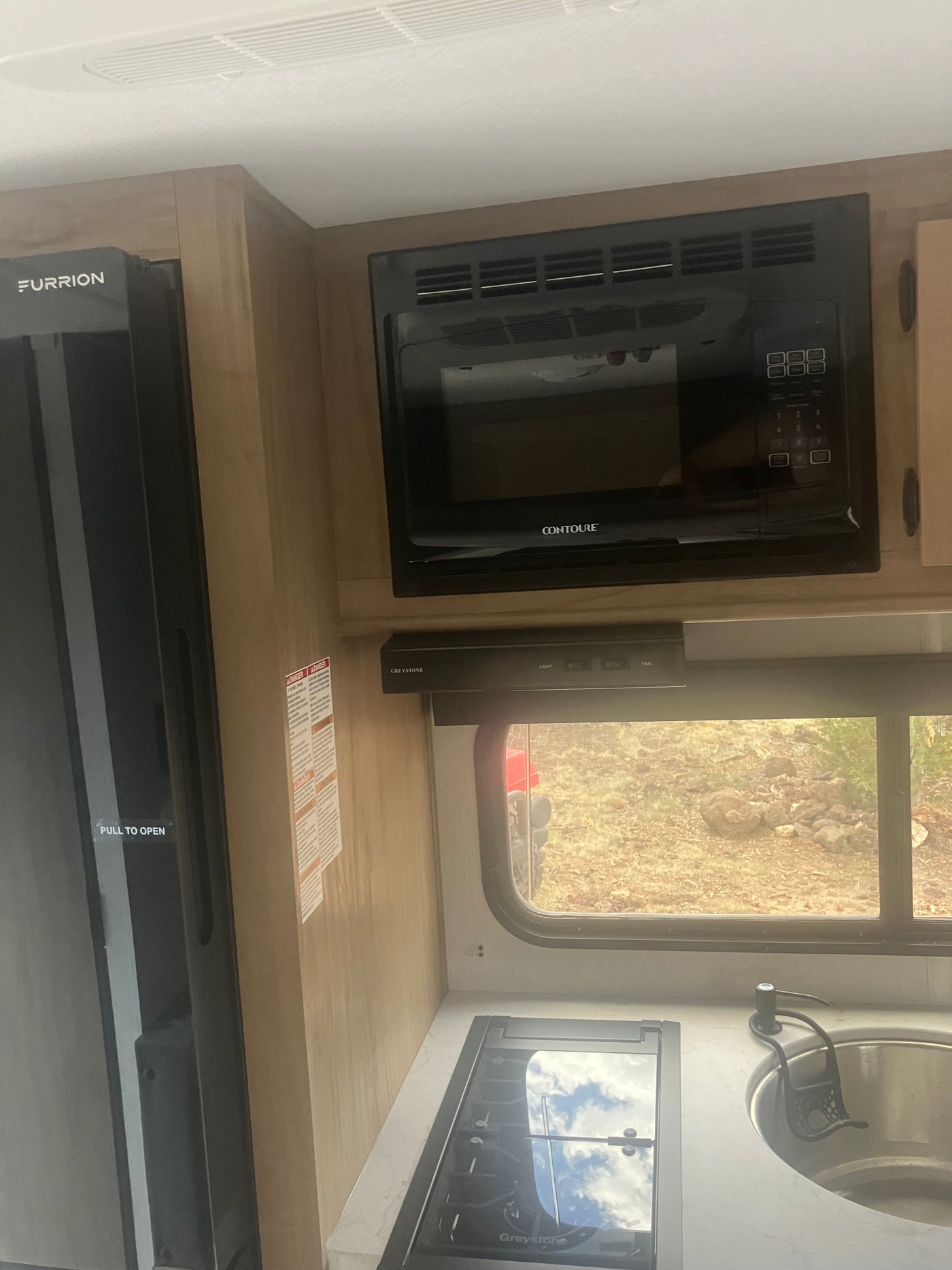 Compact rv rental kitchen: black refrigerator, microwave, gas stovetop, and sink. Efficient galley setup for travel adventures. — photo 12